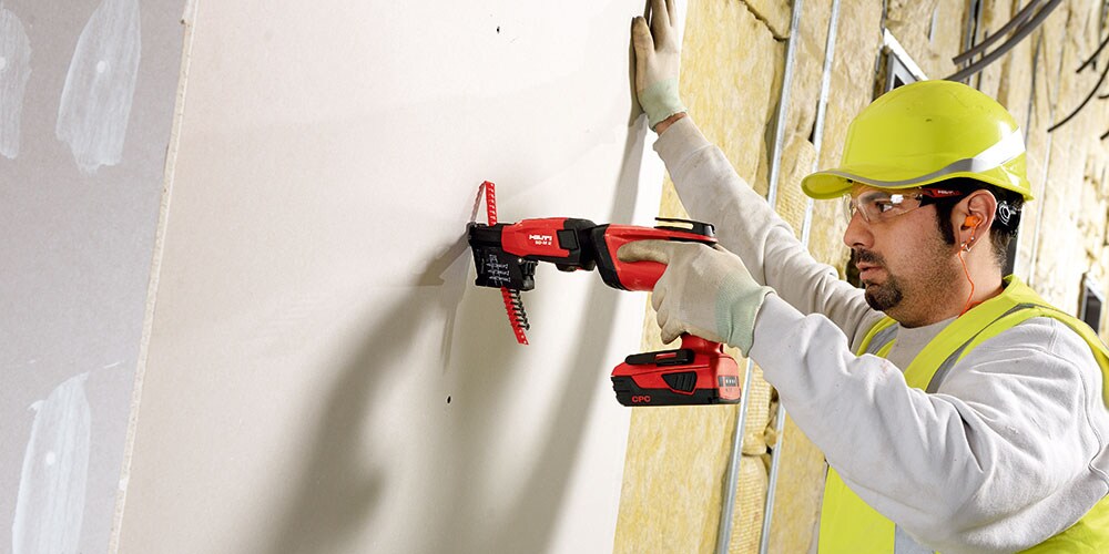 Homme sur un chantier pose des cloisons avec une visseuse et un chargeur de vis en bande