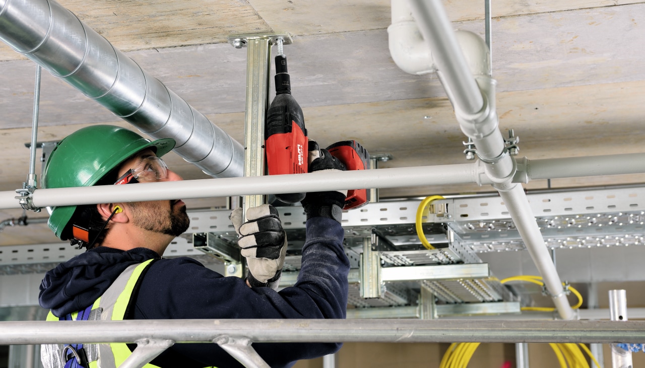 Un ouvrier fixe dans un plafond en béton avec une visseuse Hilti