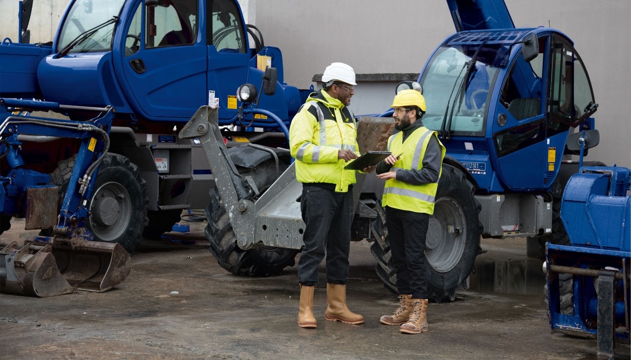 Deux ouvriers discutent au pied d’un engin de chantier