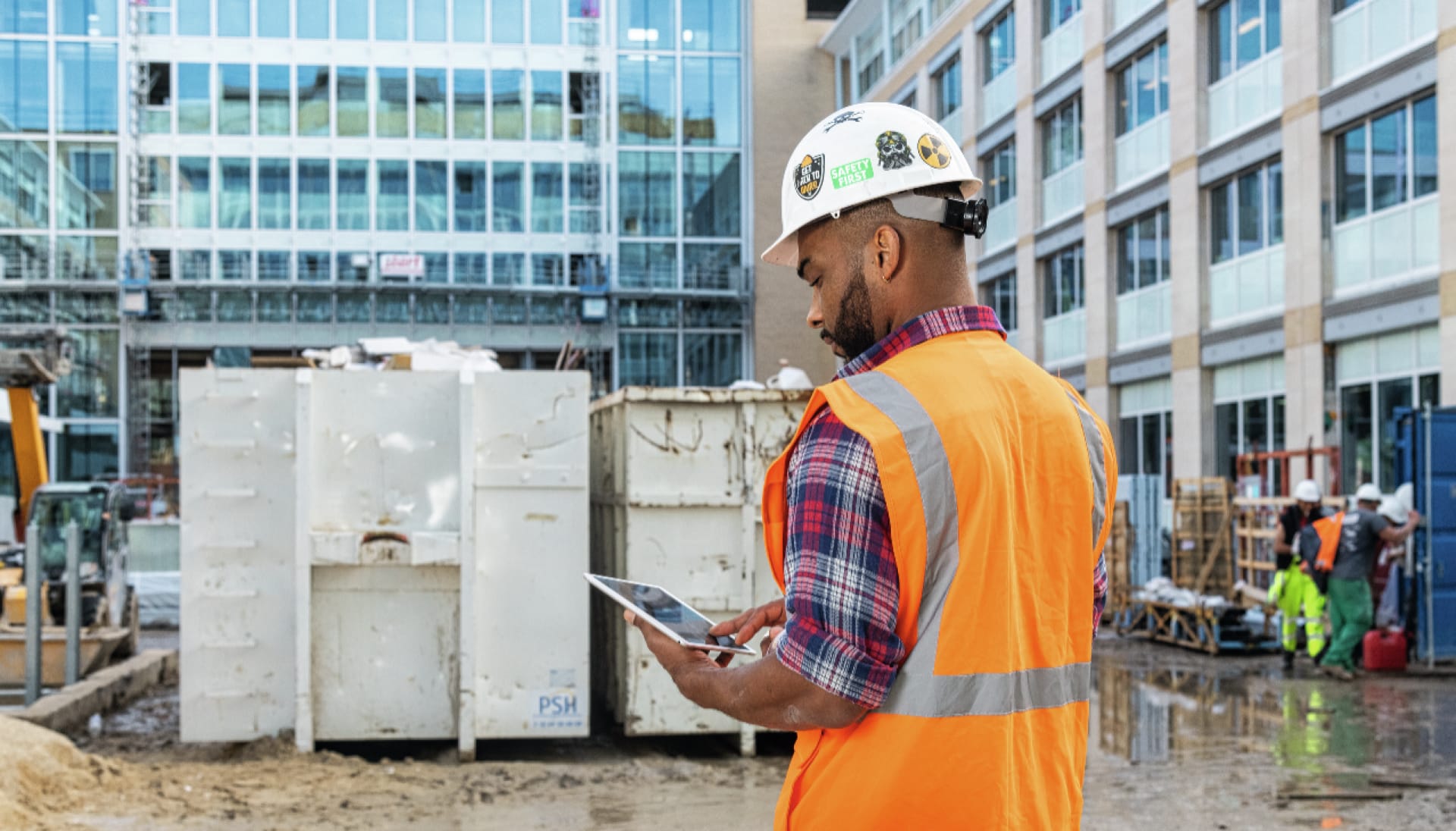 Un homme sur un chantier avec un casque et une veste de sécurité consulte une tablette avec l'application Fieldwire